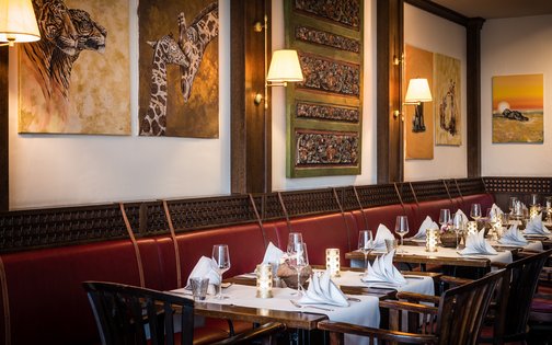 Elegant gedeckte Tische im Restaurantbereich des Park-Hotel Hagenbeck mit afrikanischen Kunstwerken an der Wand