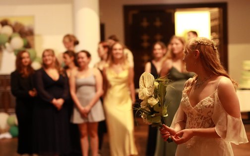 Die Braut im Vordergrund hält ihren Brautstrauß und blickt zu ihrer festlich gekleideten Gesellschaft im Ballsaal des Park-Hotels Hagenbeck in Hamburg.