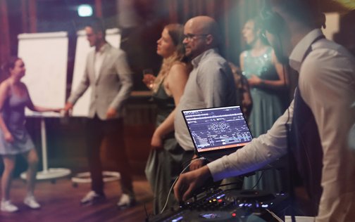 Der DJ an seinem Mischpult im Vordergrund sorgt für Stimmung bei den Hochzeitsgästen im bunt beleuchteten Saal des Park-Hotels Hagenbeck in Hamburg.